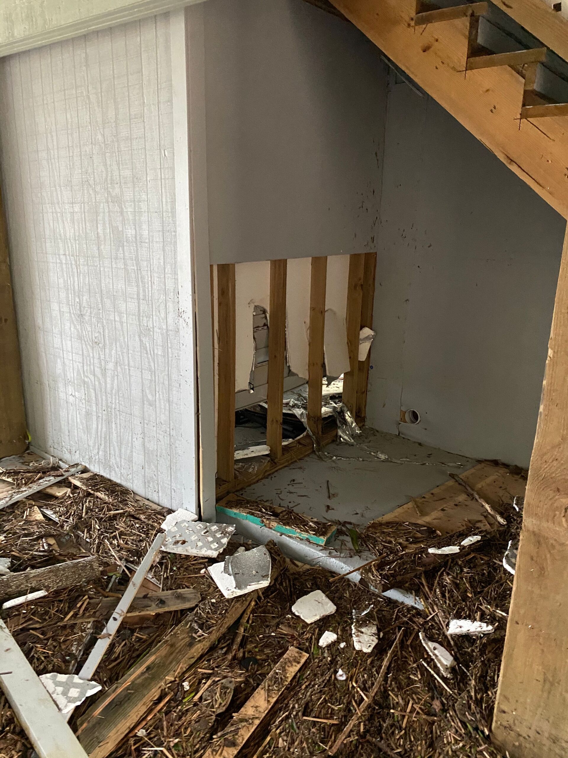 A room with a wooden staircase and a hole in the wall.