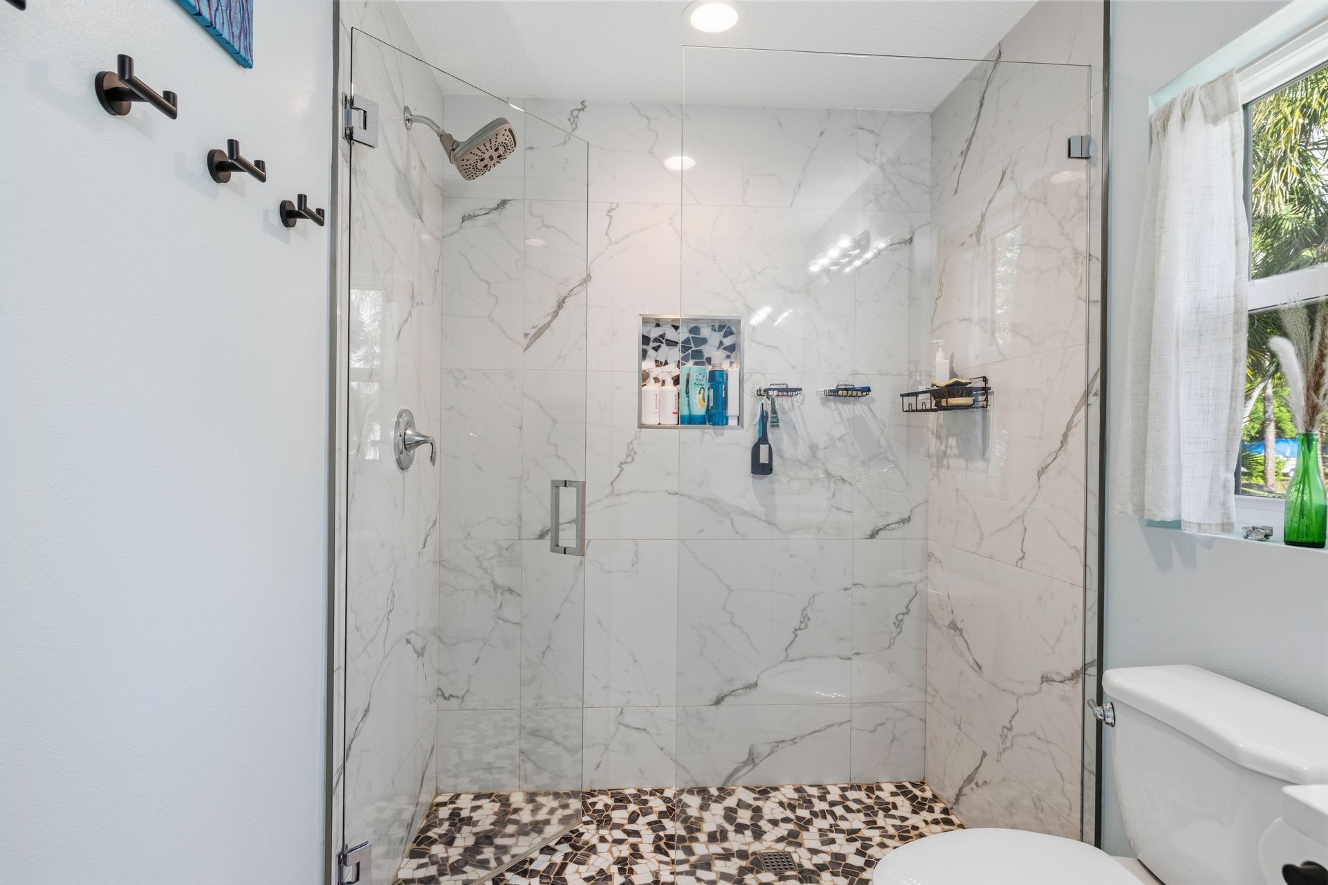 Modern bathroom shower featuring white marble-patterned tiles, a pebble floor, a glass door, and a built-in wall niche.