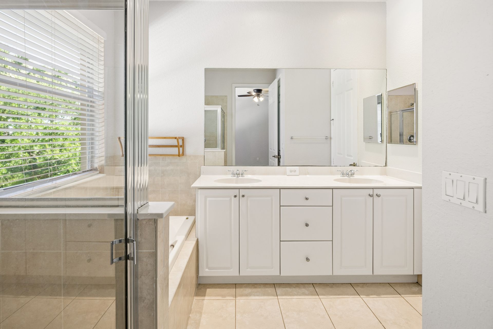 A bright, modern bathroom featuring a white double vanity, large mirror, and a glass-enclosed shower with tiled floors.