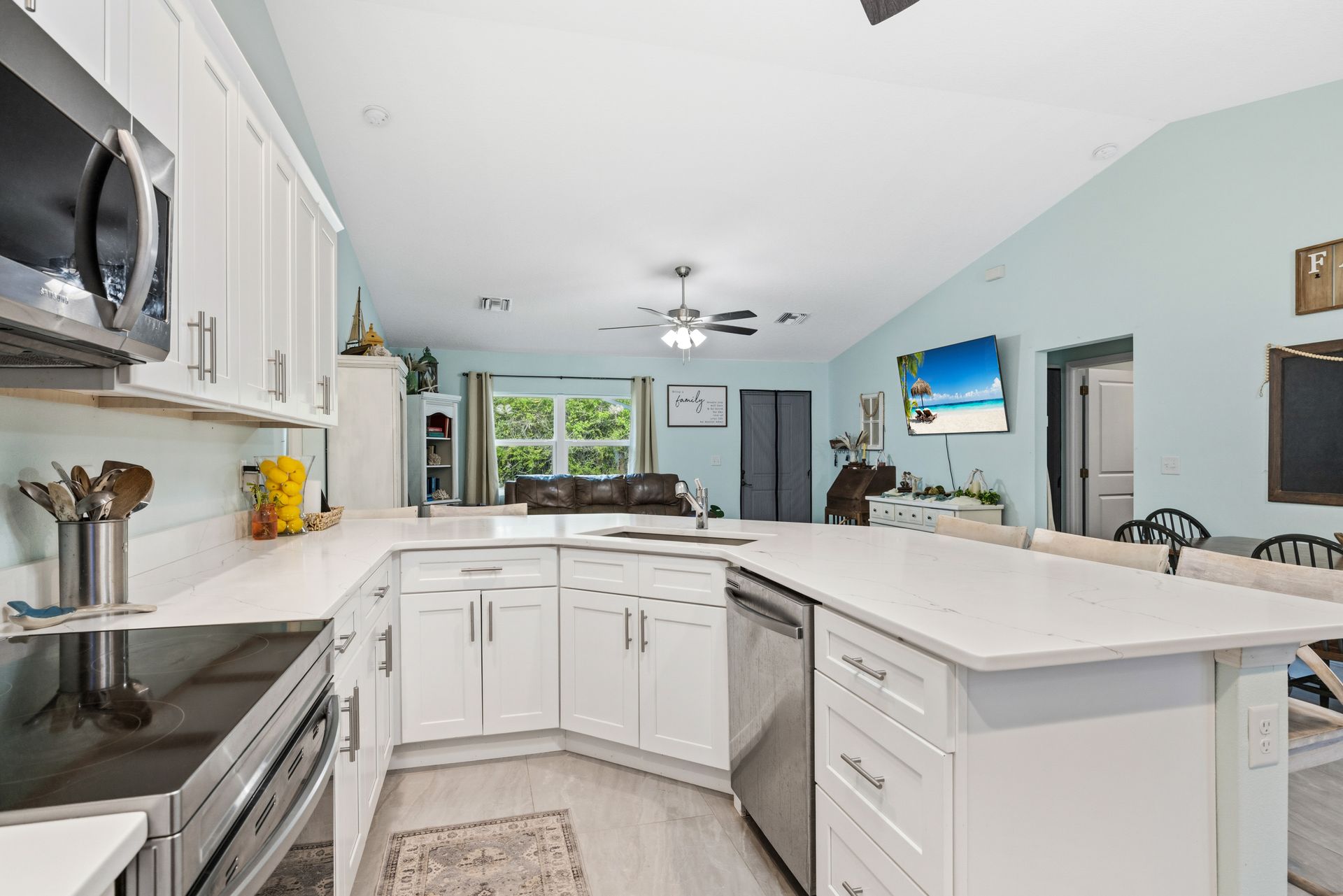 A bright, modern kitchen with white cabinets, light countertops, and stainless steel appliances in an open-concept room.