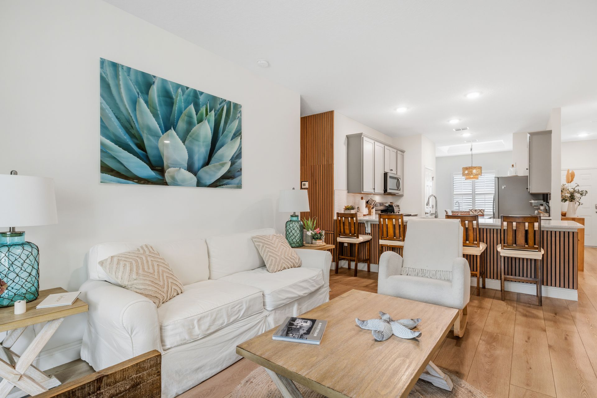 A light-filled, open-plan living room with a white sofa, coffee table, and an armchair facing a modern kitchen island.