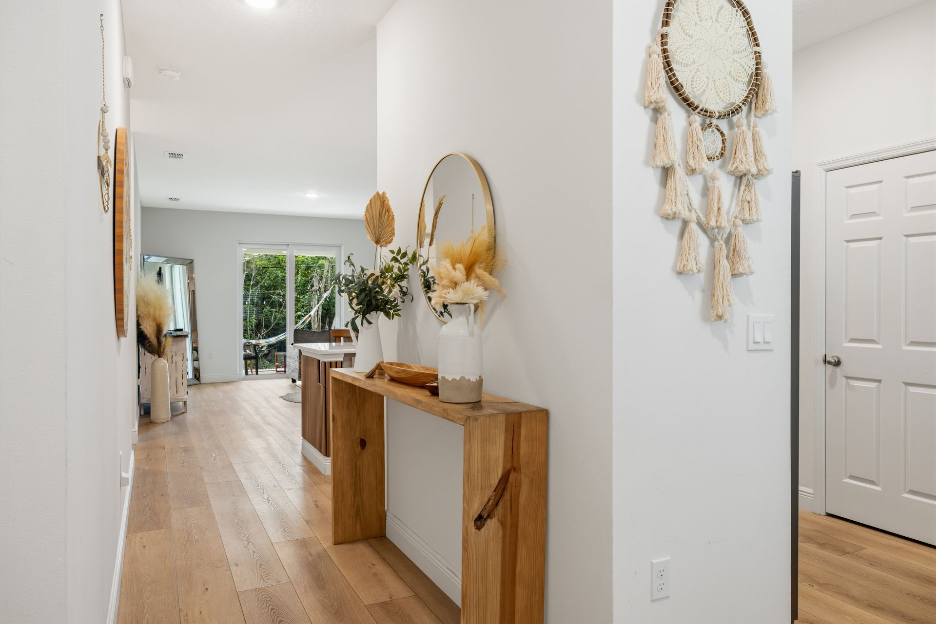 A modern entryway featuring light wood flooring, a minimalist wood console table with dried flowers, and a wall dreamcatcher.