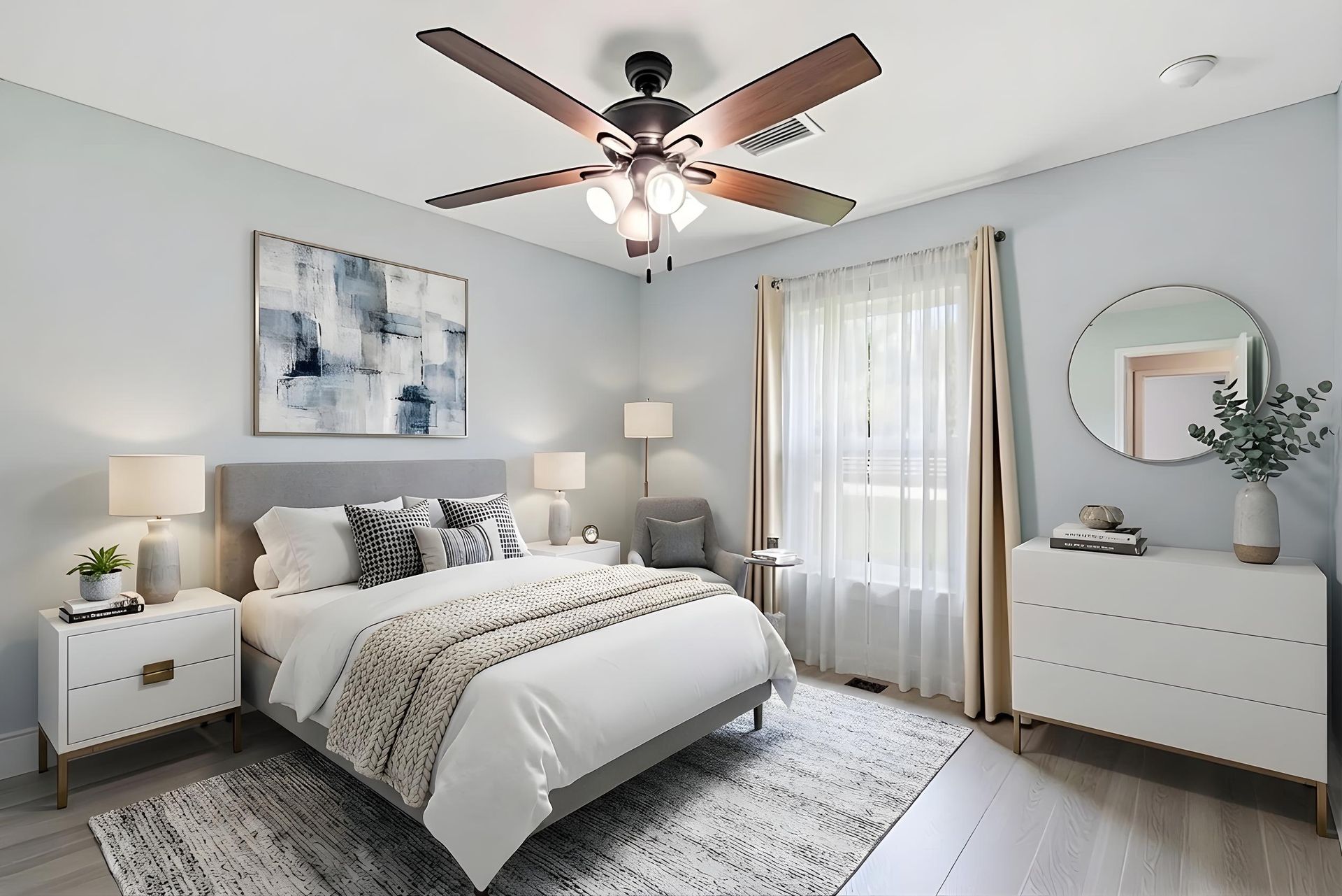 Modern bedroom with a gray upholstered bed, white dresser, large round mirror, textured rug, and ceiling fan.