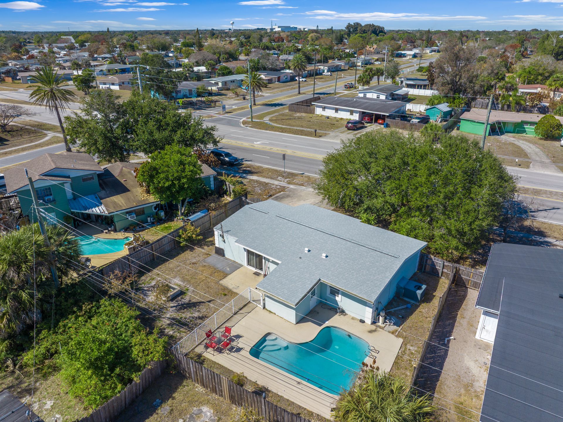 Aerial view of a light blue residential house with a gray roof and backyard swimming pool in a neighborhood.