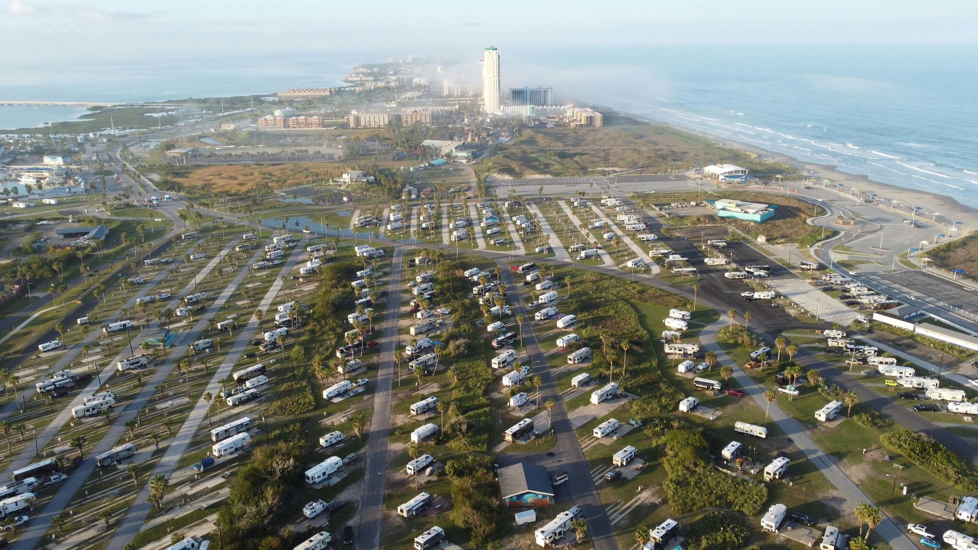 Aerial view of RV park near beach with ocean and distant buildings.
