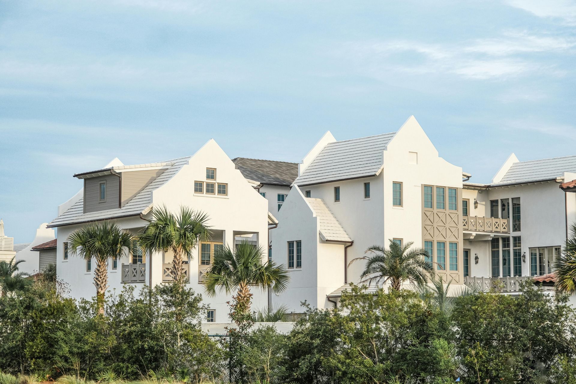 White beach houses with gabled roofs, balconies, and palm trees against a blue sky.