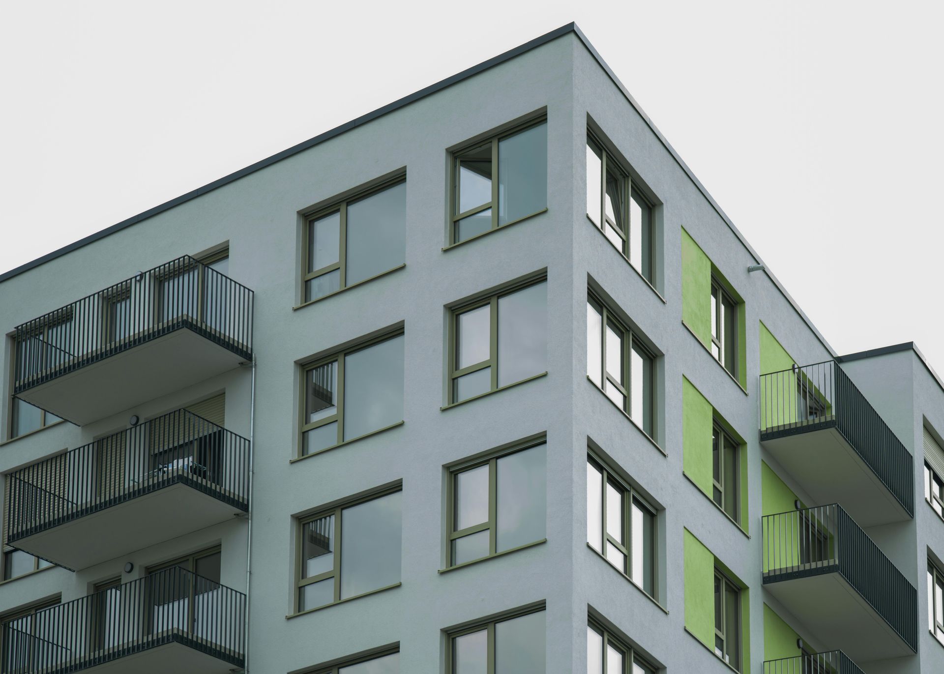 Modern white apartment building with balconies and green accents against a gray sky.