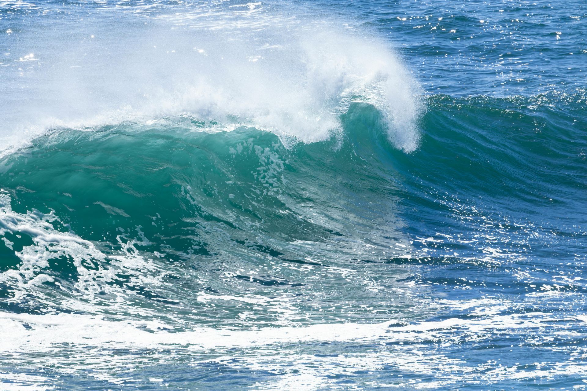 Large teal ocean wave curling and crashing with white spray