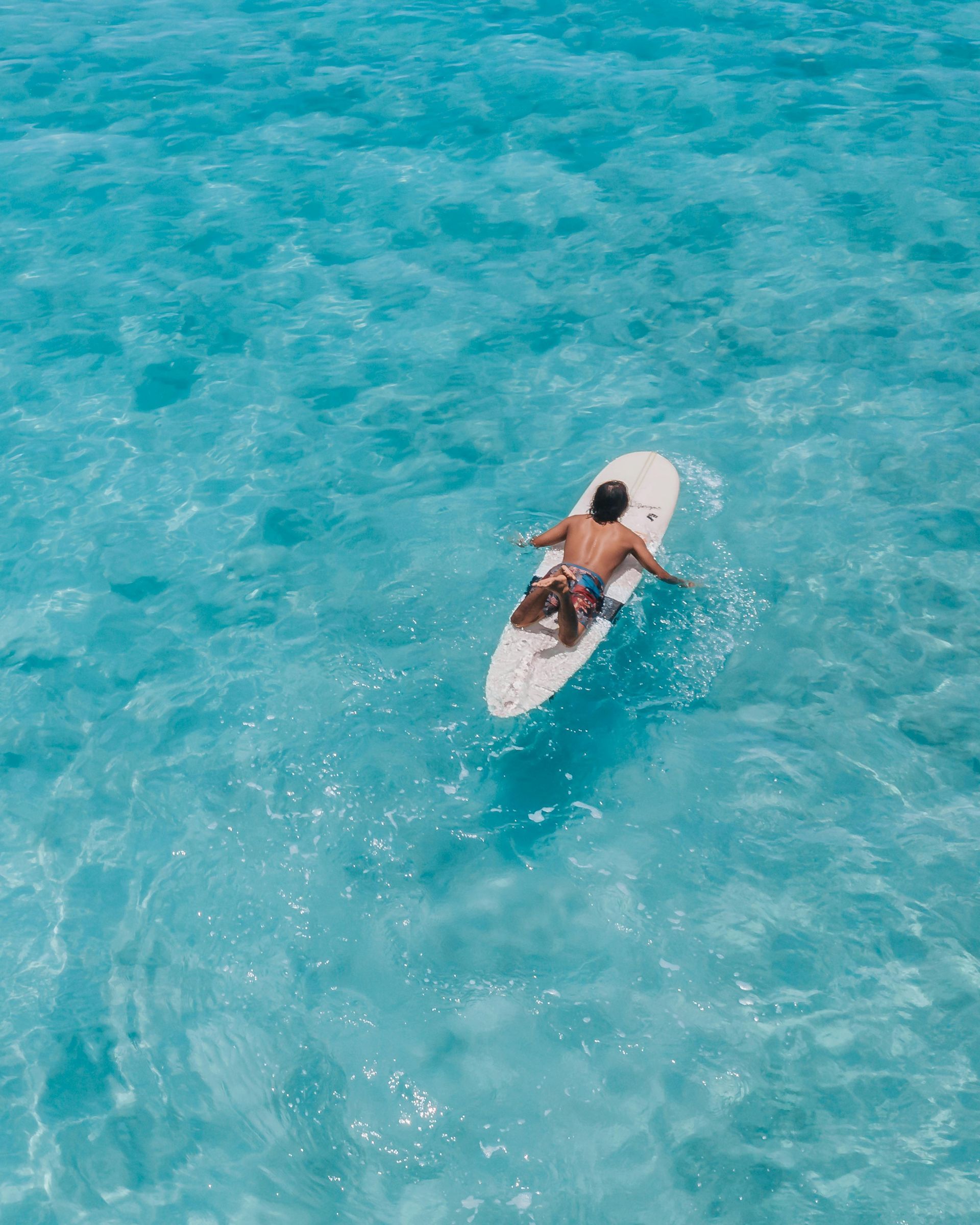 Person paddling a white surfboard on bright turquoise water