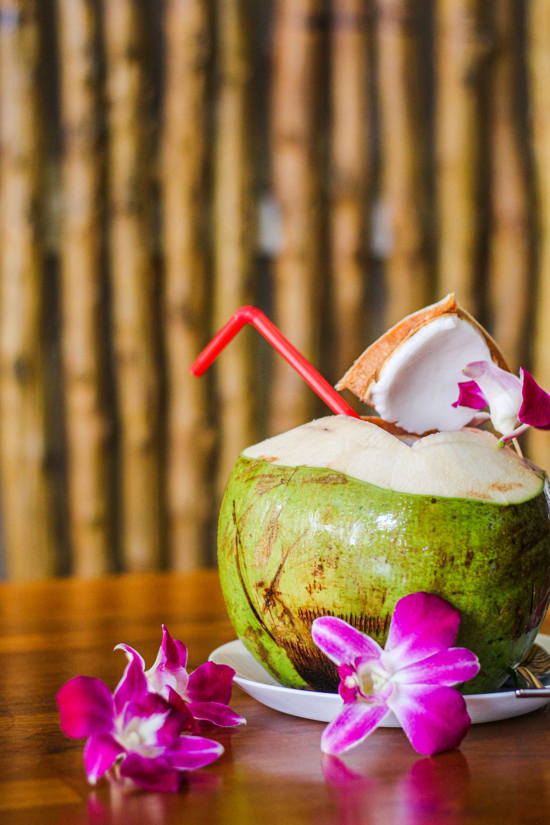 Coconut drink with red straw, orchid flowers on wood table.