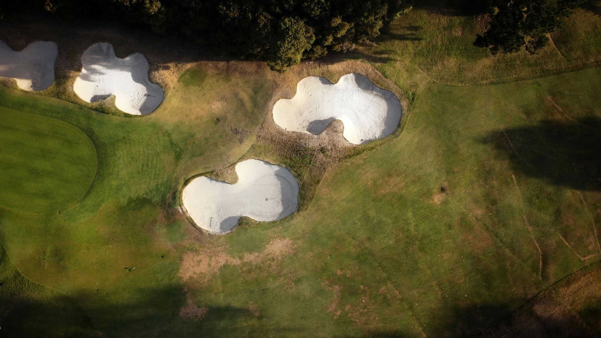Overhead view of a golf course, showing three sand traps filled with white sand on a green lawn.