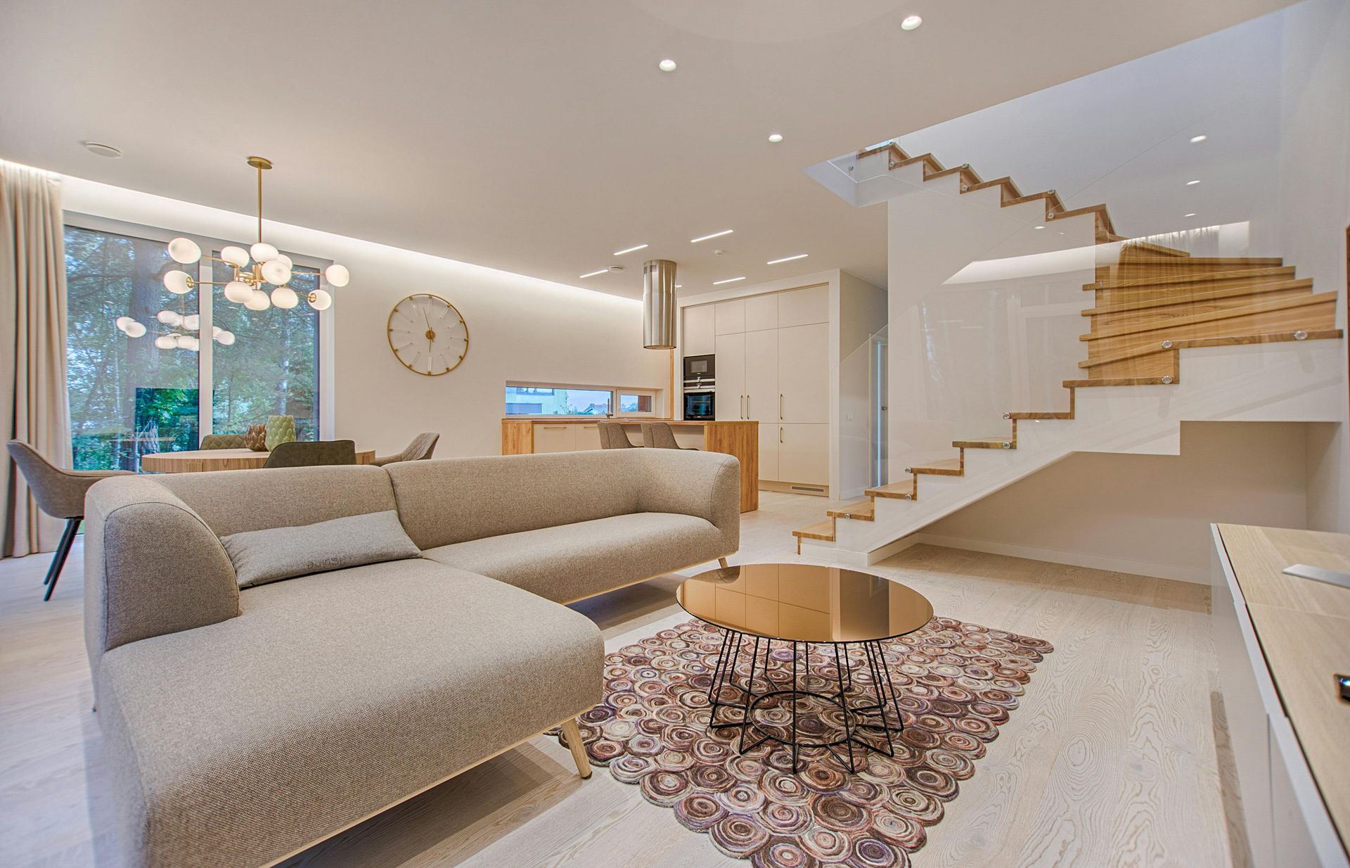 Modern living room with sectional sofa, wooden staircase, and a round coffee table.