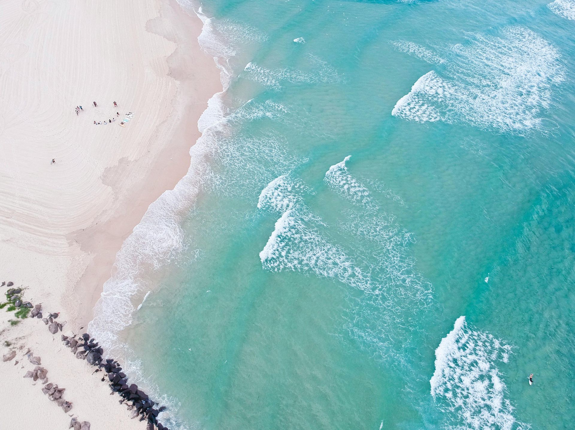 Aerial view of a sandy beach with turquoise water and small waves breaking on the shore.