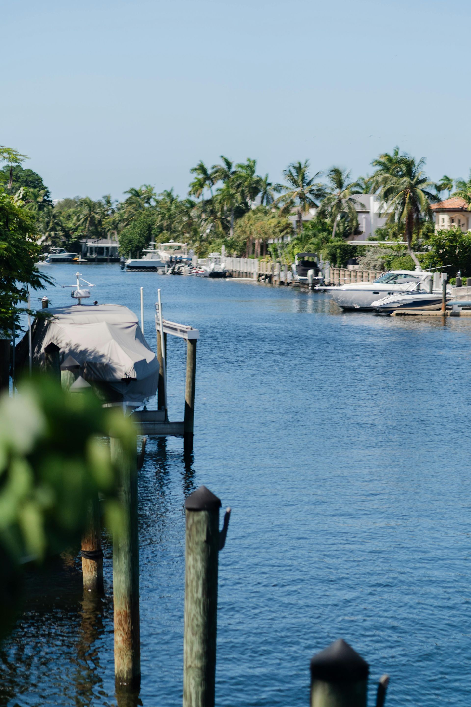 Water canal lined with docks and boats, palm trees, and waterfront homes. Sunny blue sky.