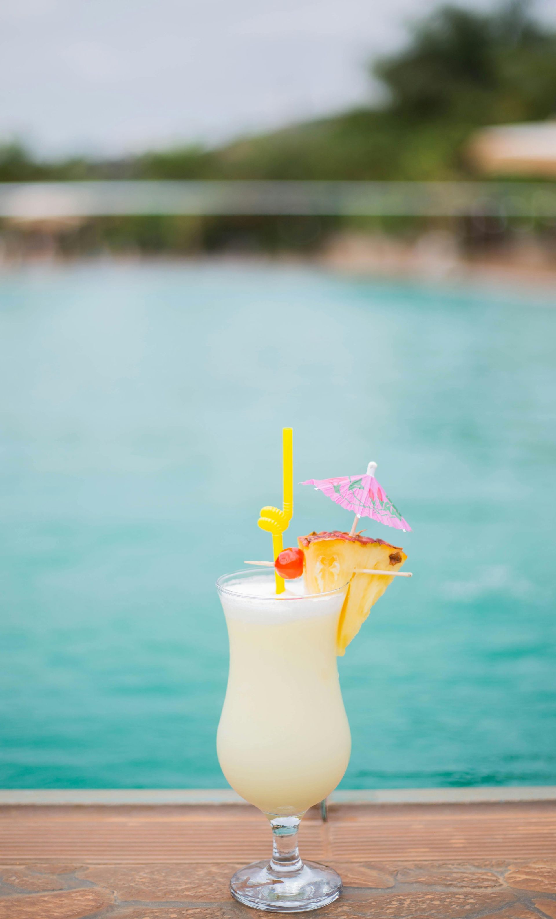Pina colada cocktail with garnish on a wooden surface by a pool.