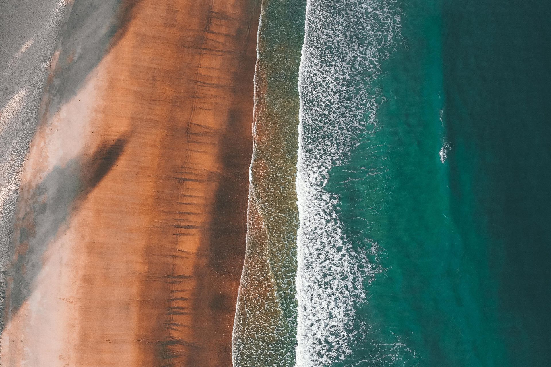 Aerial view of beach with brown sand meeting turquoise ocean and white waves.