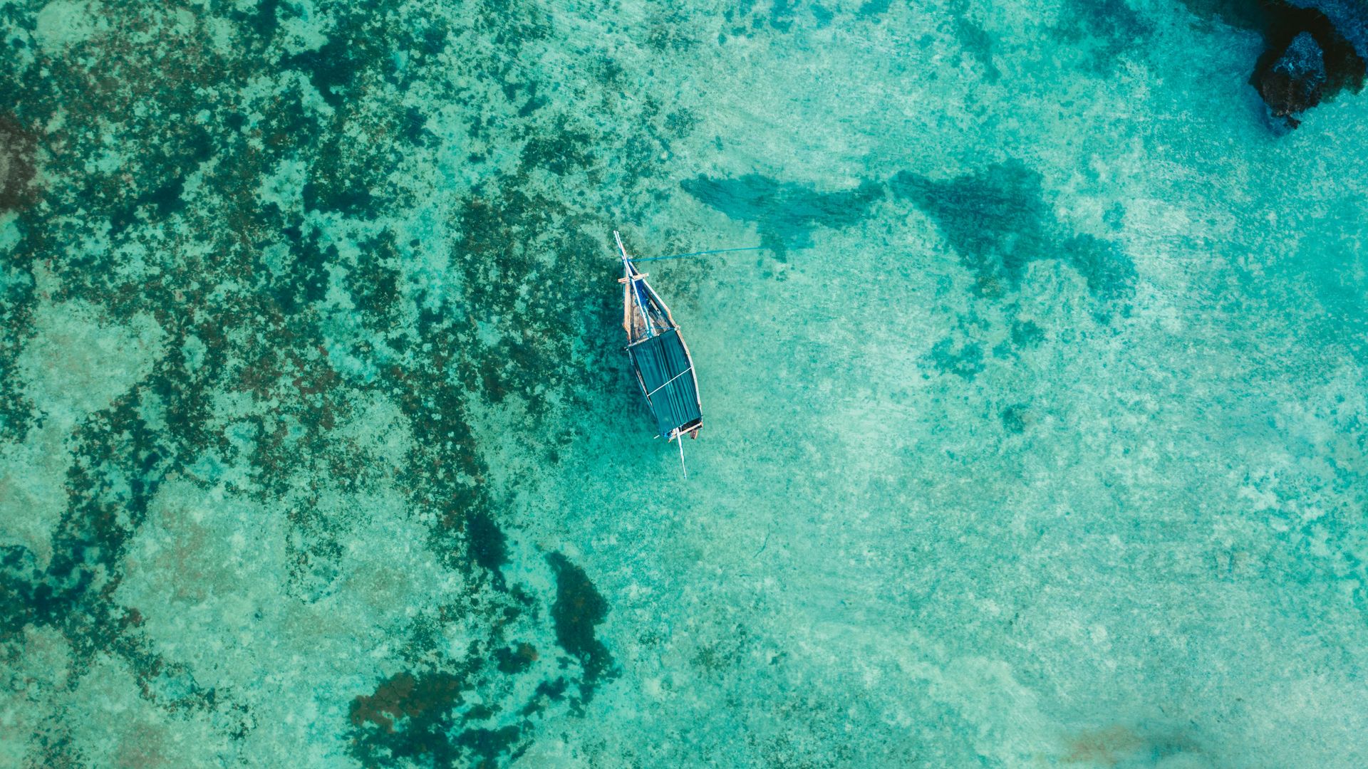 A small boat floats in clear, shallow turquoise water over a patterned seabed viewed from above.