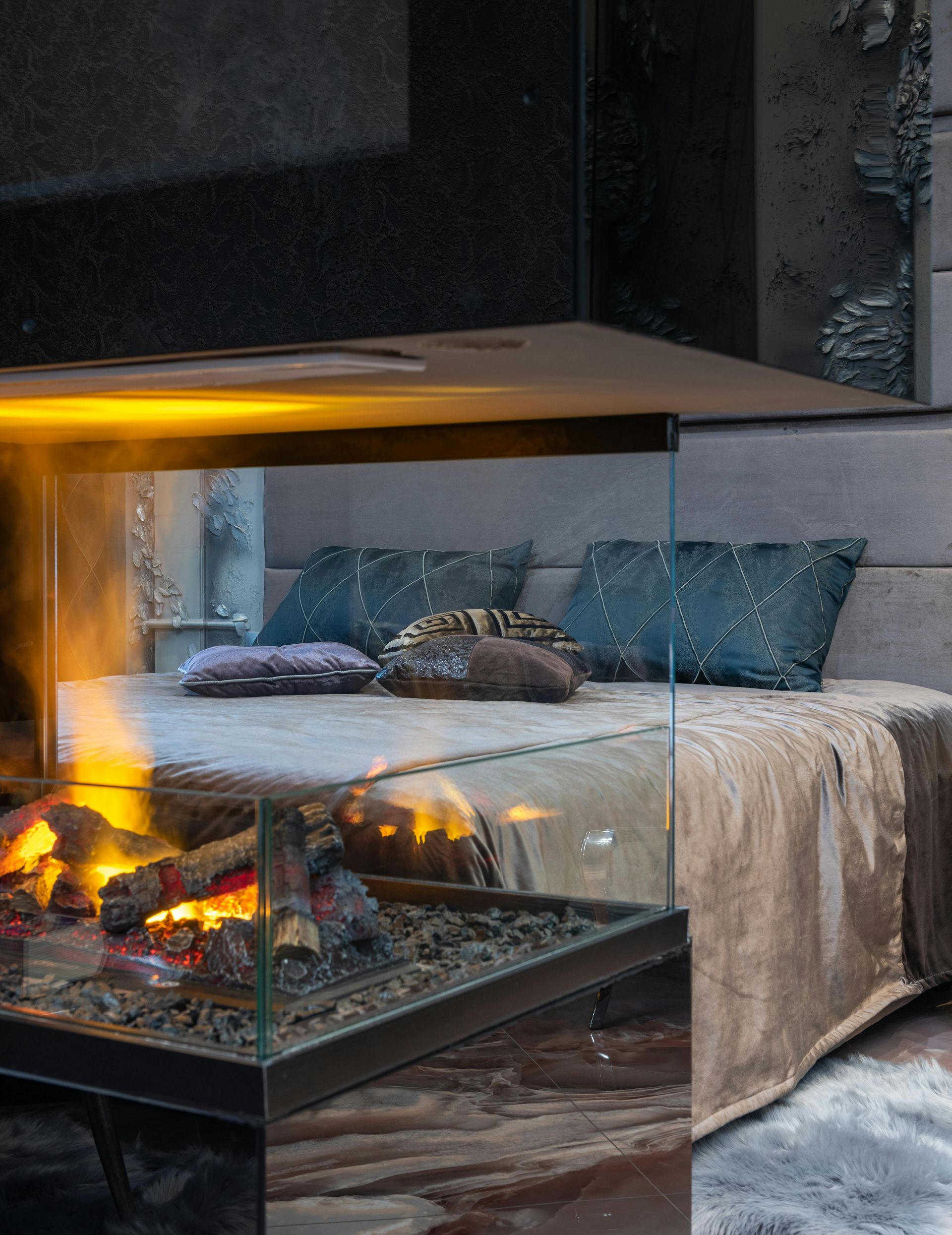 Fireplace with flames next to a bed with pillows and a blanket.