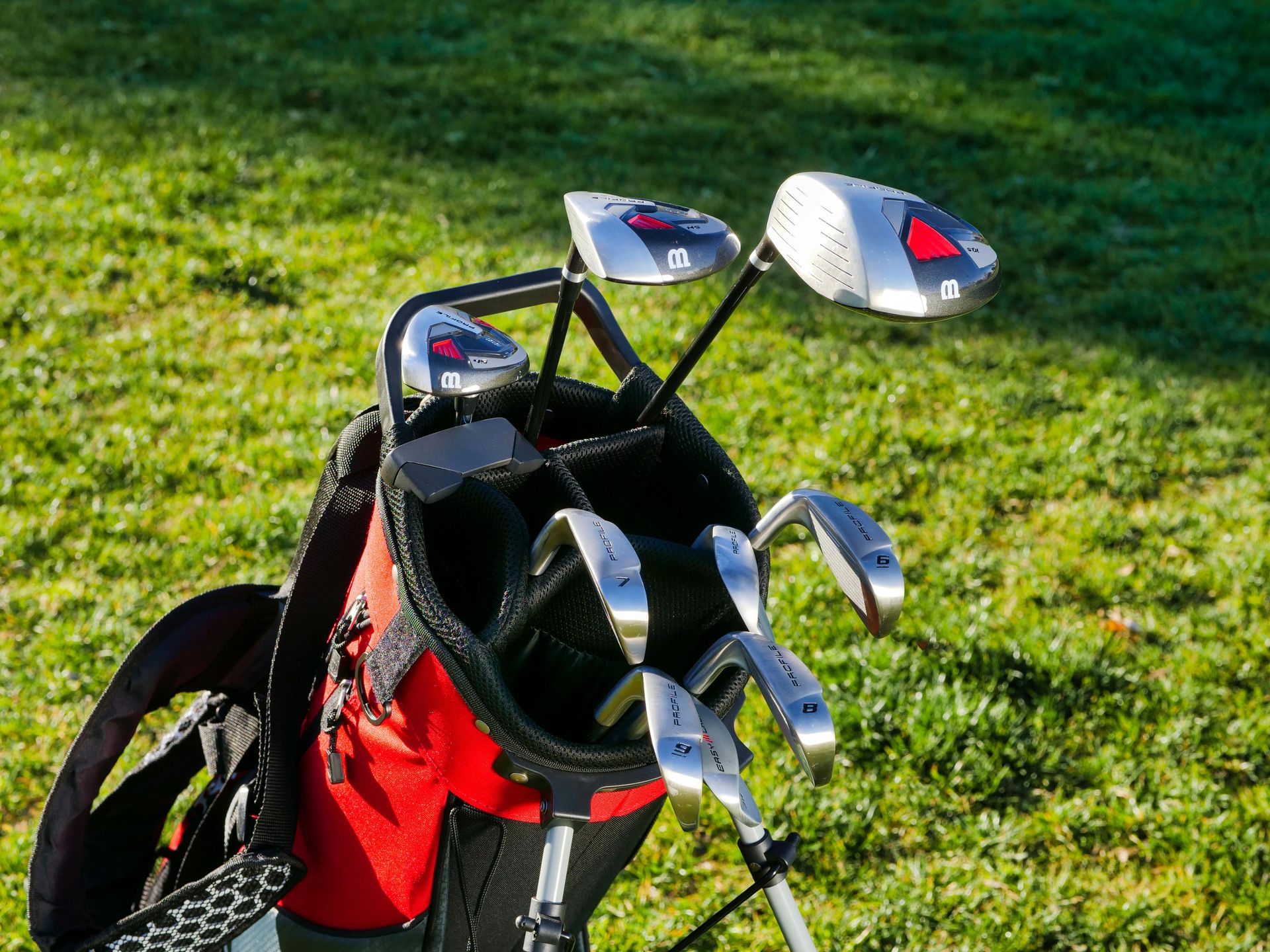 Red golf bag with clubs on green grass.