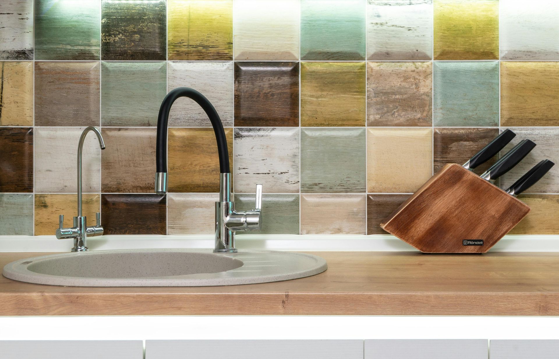 Kitchen sink with multicolored square tile backsplash, and knife block.