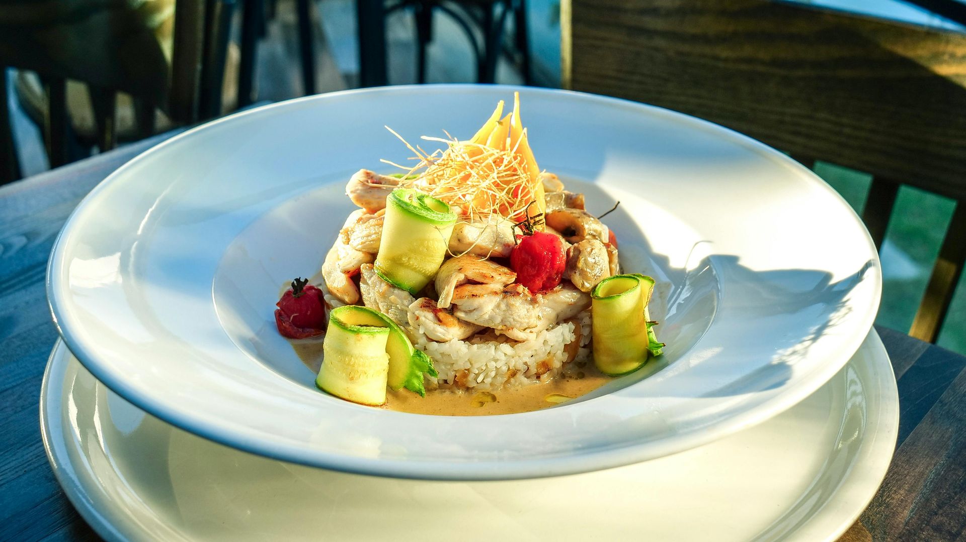 Gourmet plate of rice, chicken, zucchini rolls, and garnish, on a white plate, outside setting.