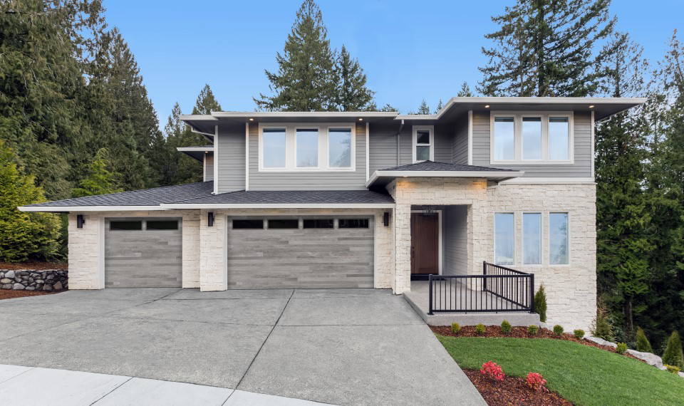 Modern two-story gray house with a three-car garage, front porch, and landscaped yard