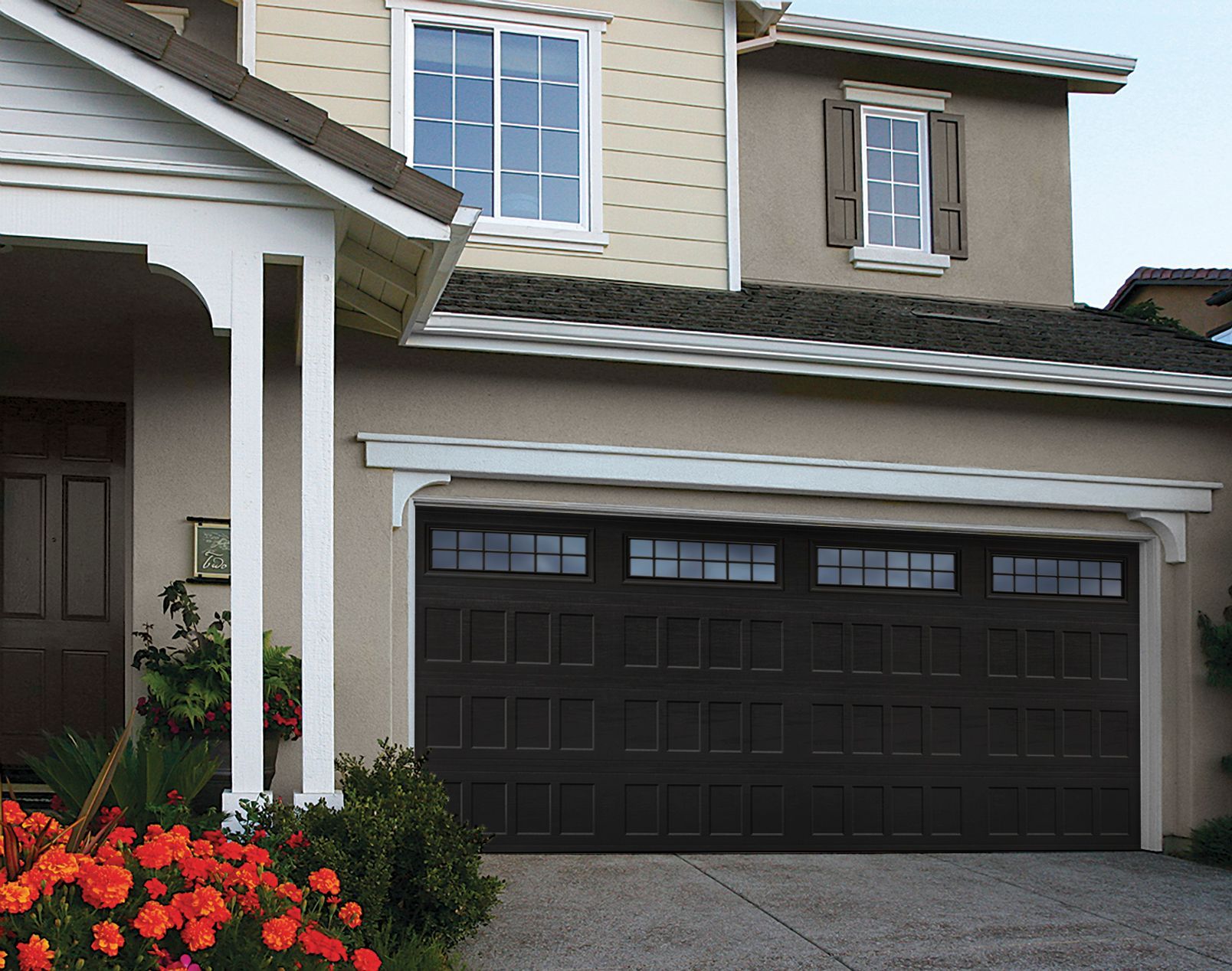 Brown garage door with windows, tan house, and flowers in front.
