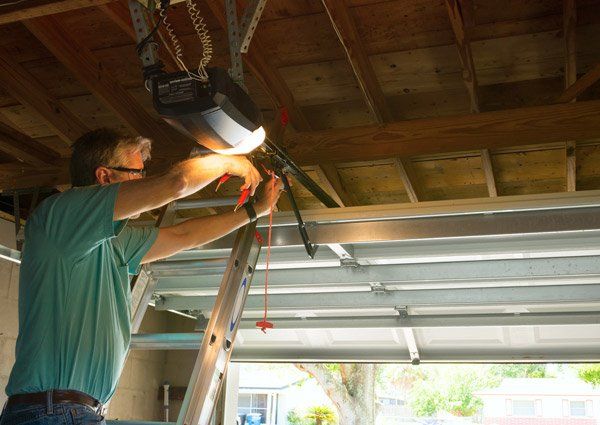 Man on a ladder repairs a garage door opener in a garage. Man on a ladder repairs a garage door opener in a garage.
