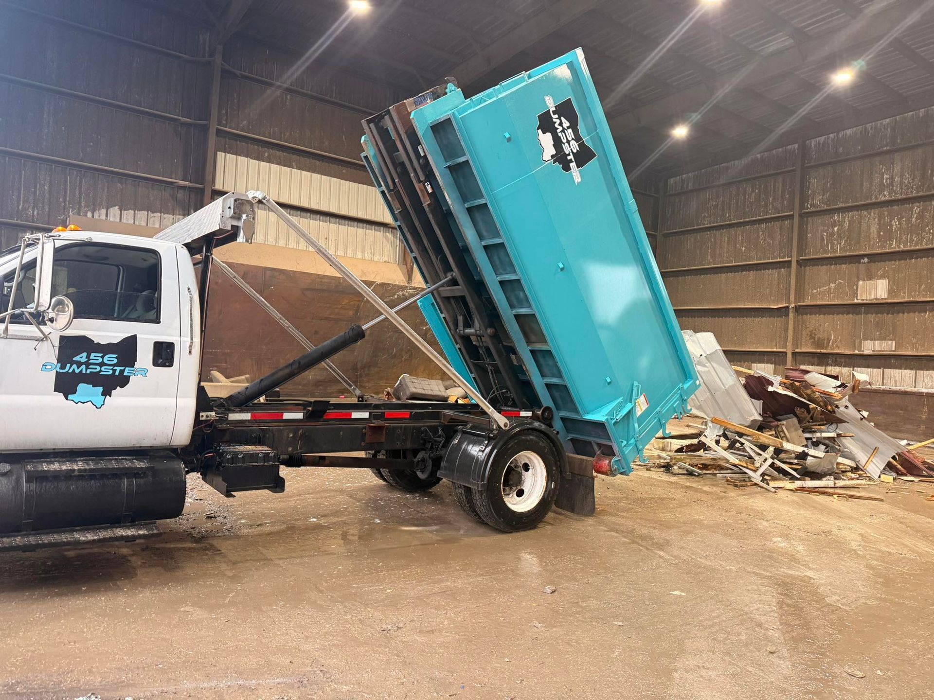 A dumpster is sitting in a gravel lot next to a truck.