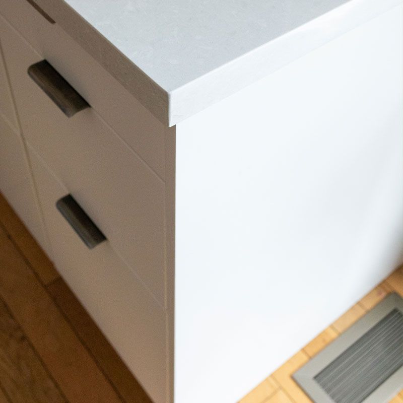 A white cabinet with black handles is sitting on a wooden floor.