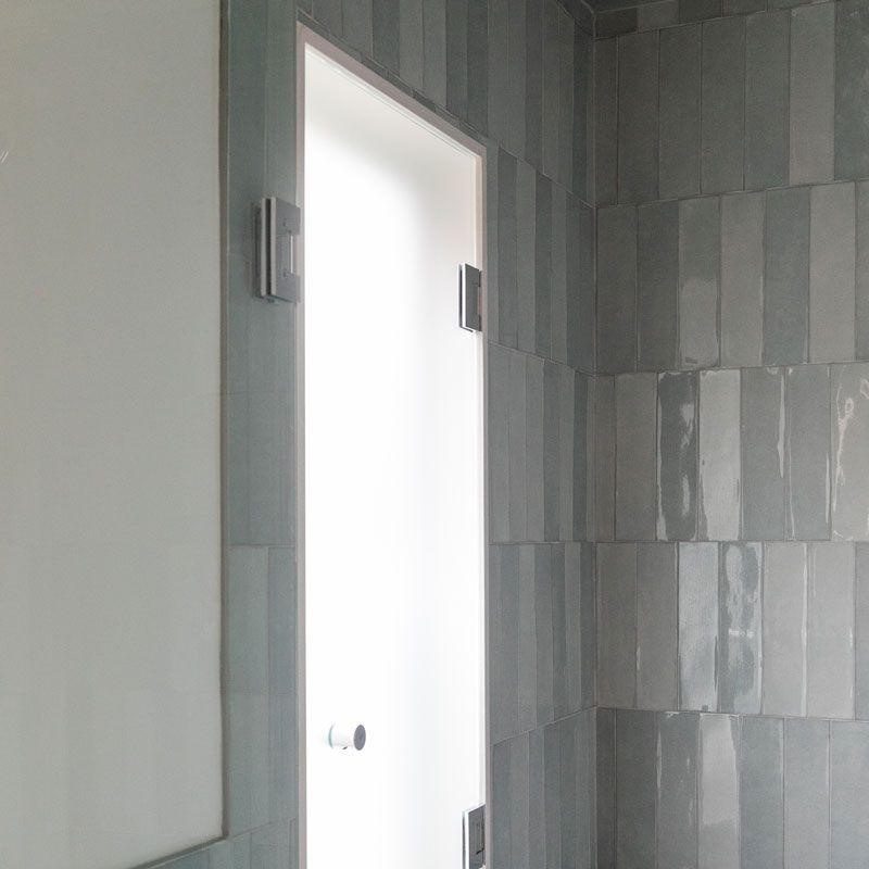A bathroom with gray tiles and a glass door.