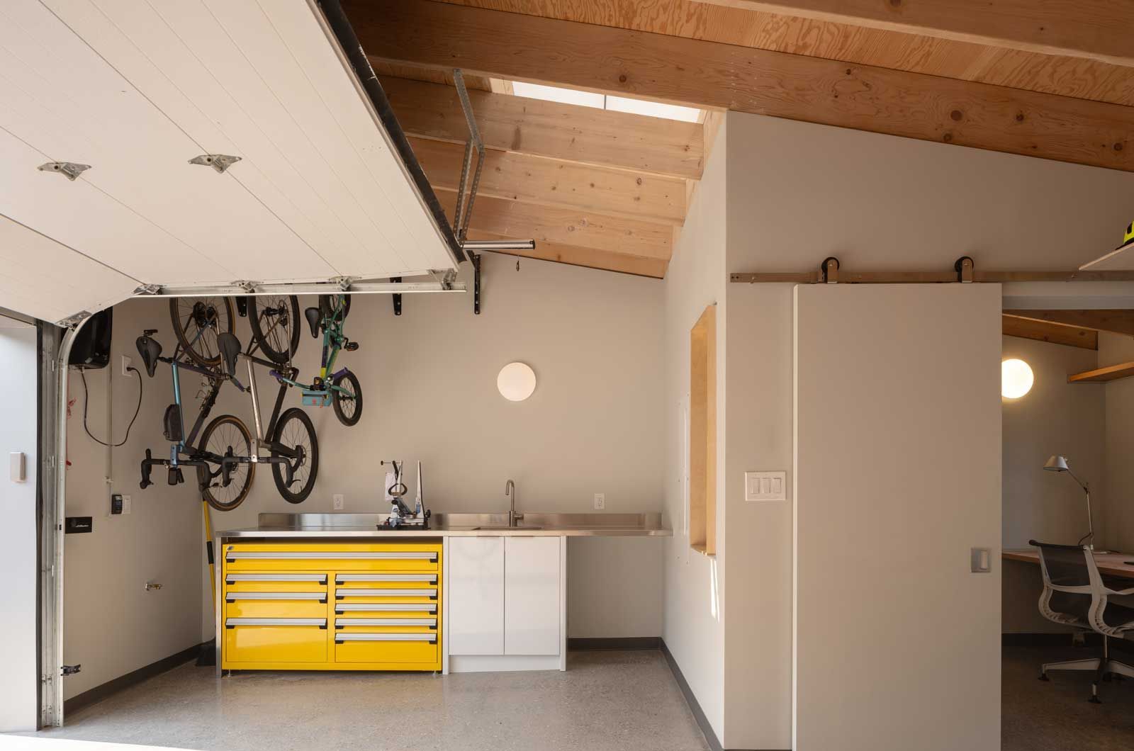 A garage with bikes hanging from the ceiling and a yellow workbench.