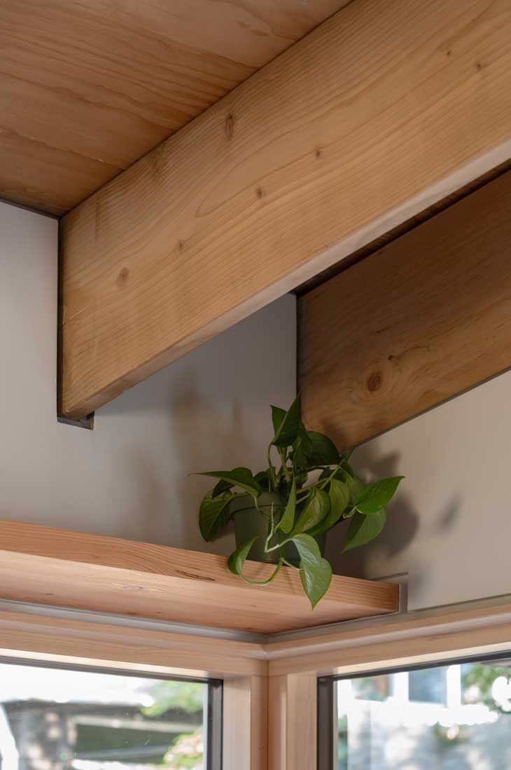 A plant is sitting on a wooden shelf next to a window.