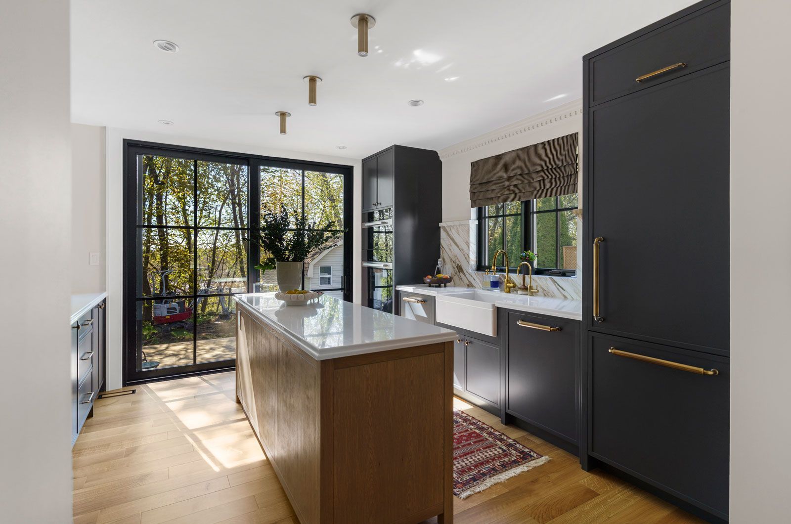 Modern kitchen with black cabinets, white counters, central island, and large windows opening to a sunlit patio