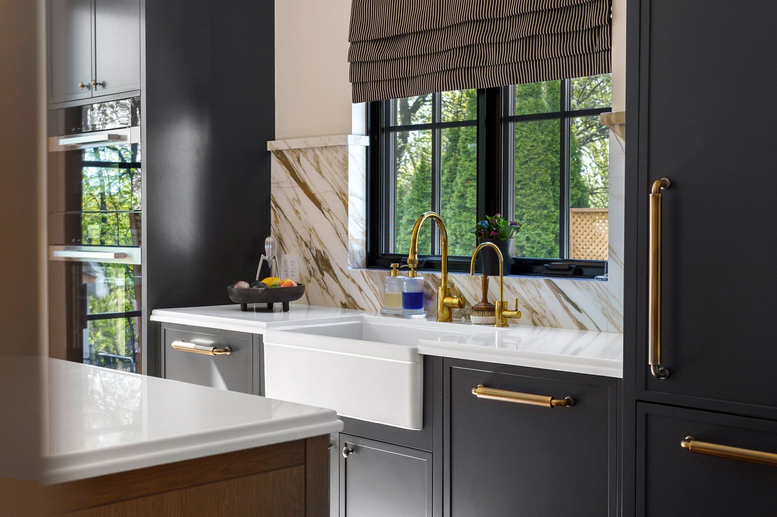 Modern kitchen with black cabinets, white marble counters, gold fixtures, and a zebra blind by the sink