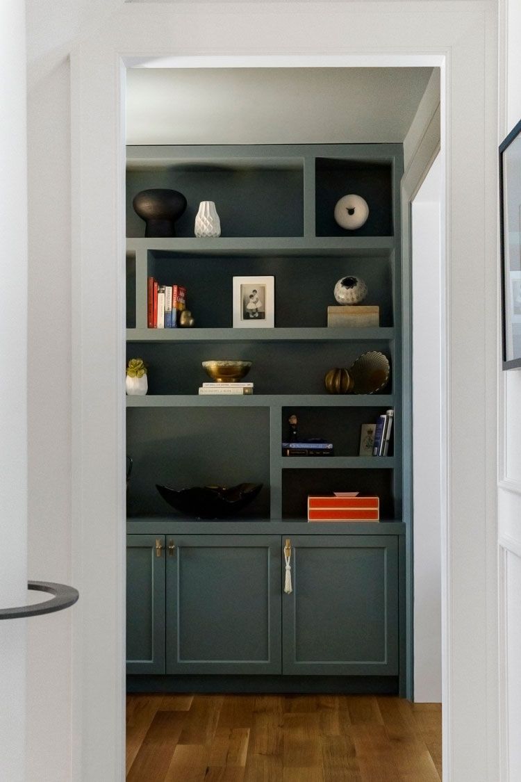 Built-in teal bookshelf with decor in a white hallway doorway