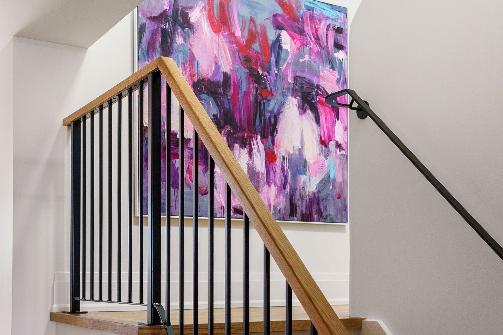 Abstract pink-purple artwork on a stair landing with wooden and black metal railing.