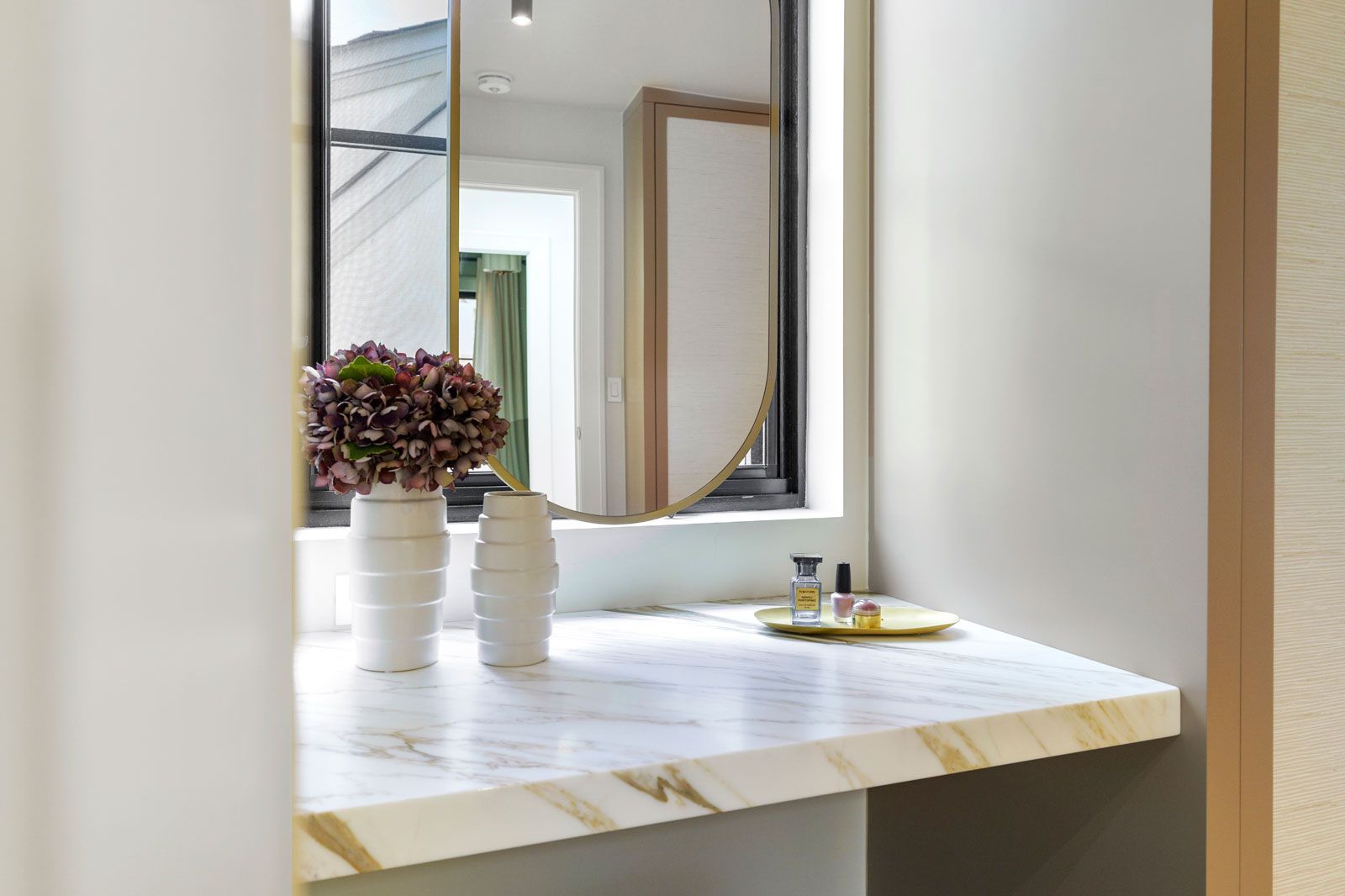 Minimalist vanity with white countertop, mirror, and small flower vase in a bright room