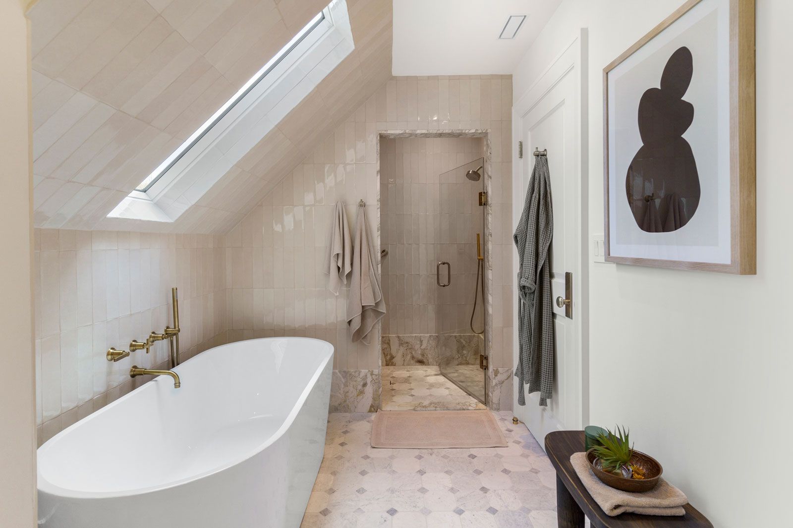 Bright white bathroom with skylight, freestanding tub, and framed wall art.
