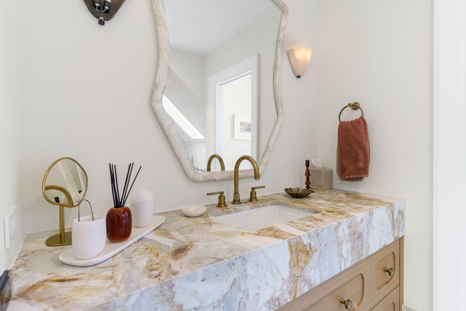 Elegant bathroom vanity with marble countertop, gold faucets, oval mirror, and wall sconce