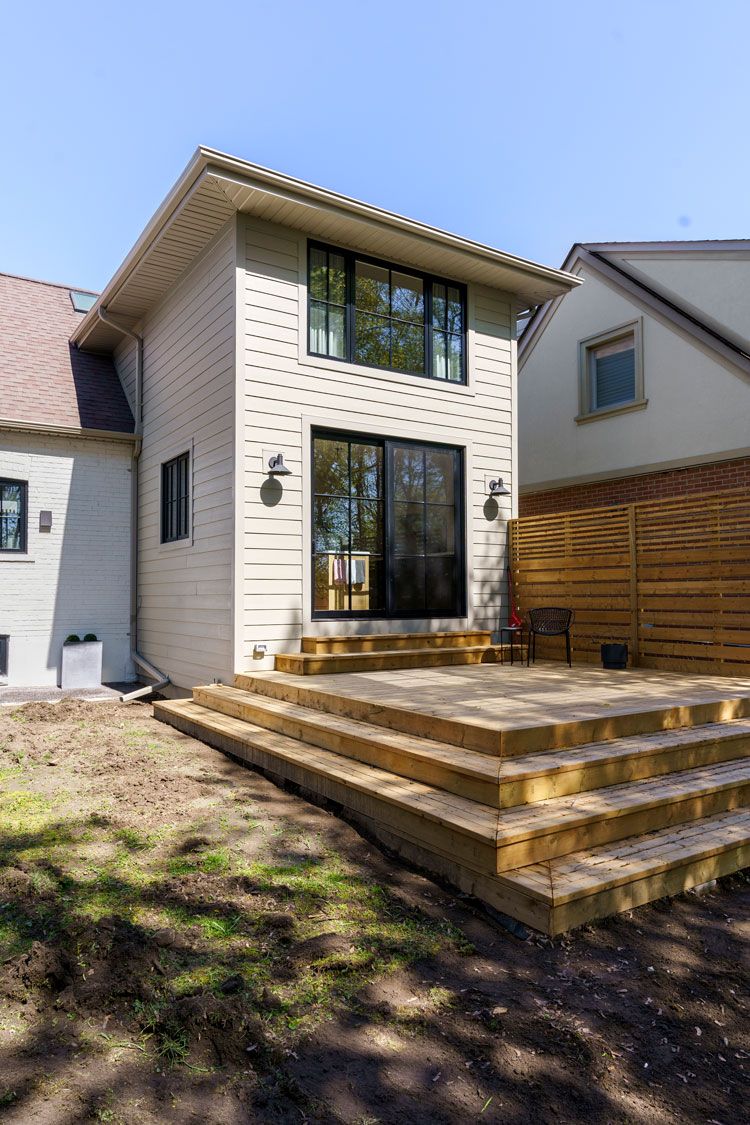 Modern two-story white house with large windows and a wooden deck in front yard