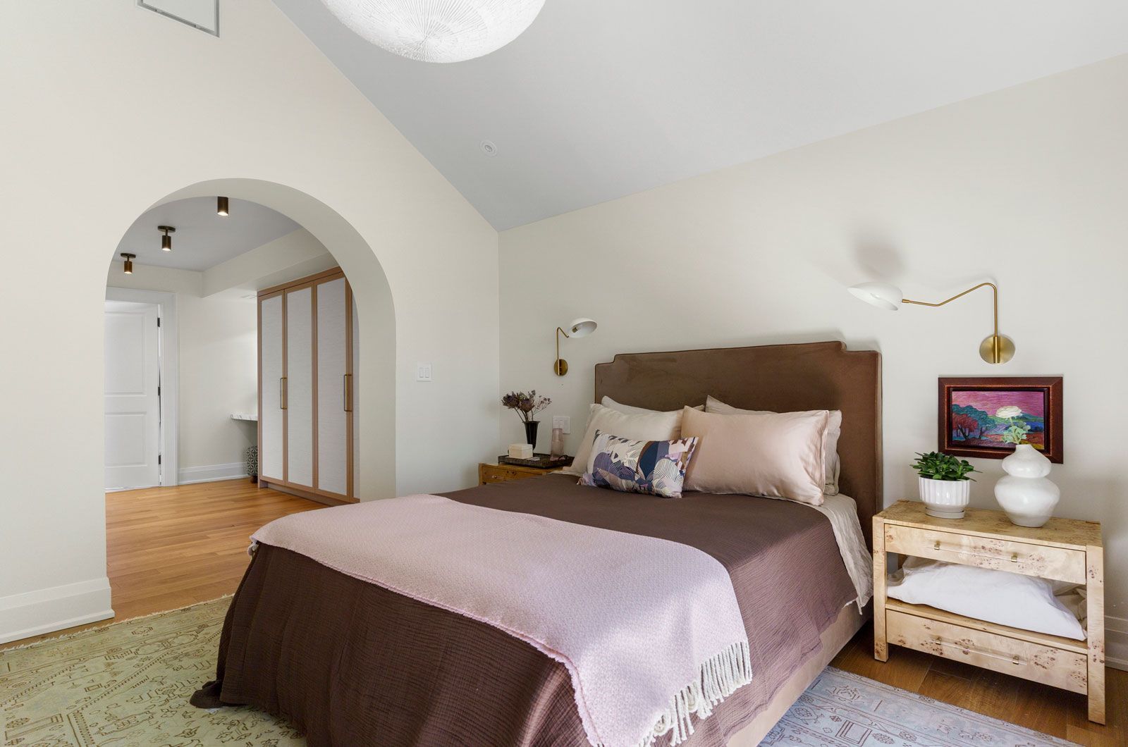 Bright bedroom with a brown bed, white nightstand, arched doorway, and soft neutral decor