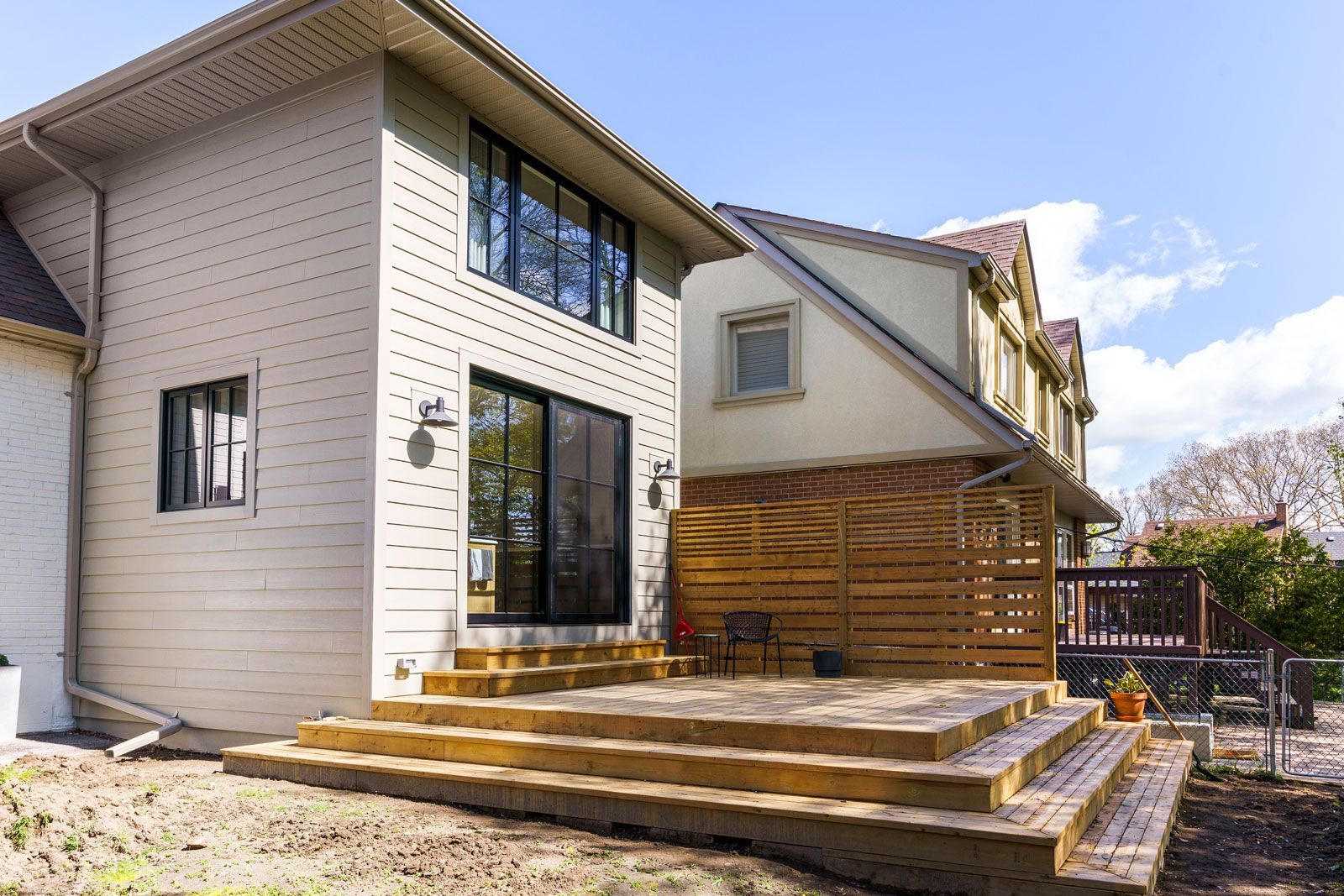 Modern two-story house exterior with large windows, wood siding, and stepped backyard patio