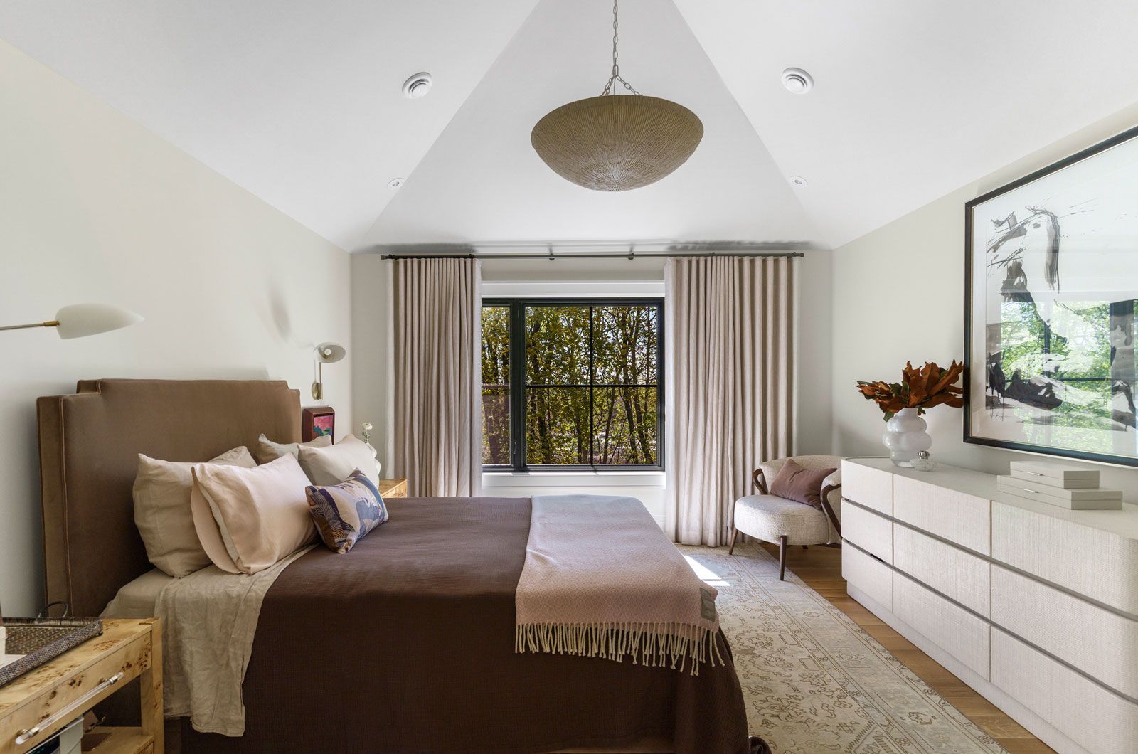 Bright bedroom with a bed, dresser, window curtains, and wall-mounted TV