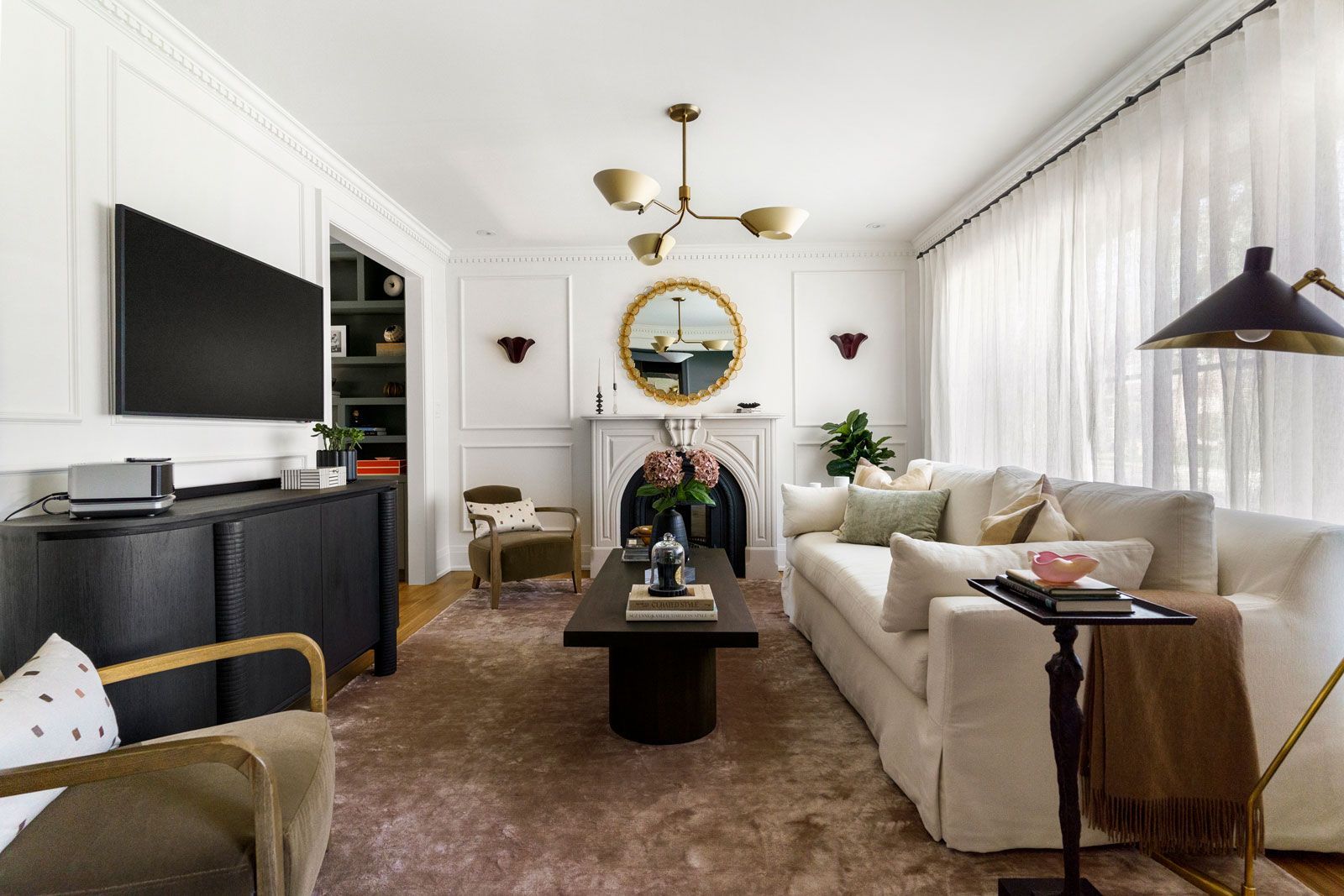 Bright living room with white sofa, black coffee table, wall TV, and gold chandelier
