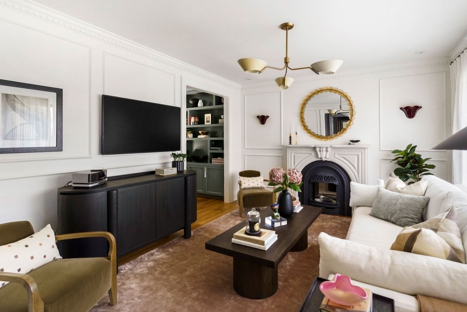Bright living room with white sofa, dark coffee table, TV, fireplace, and gold mirror accents