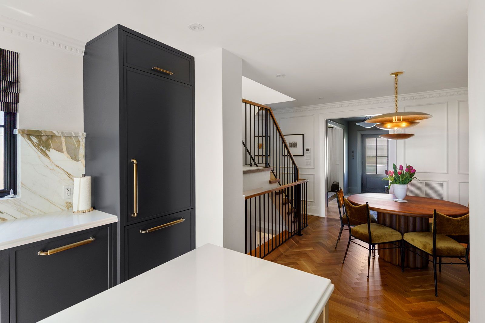 Modern kitchen and dining area with black cabinets, white countertops, wood floors, and a round table with flowers.