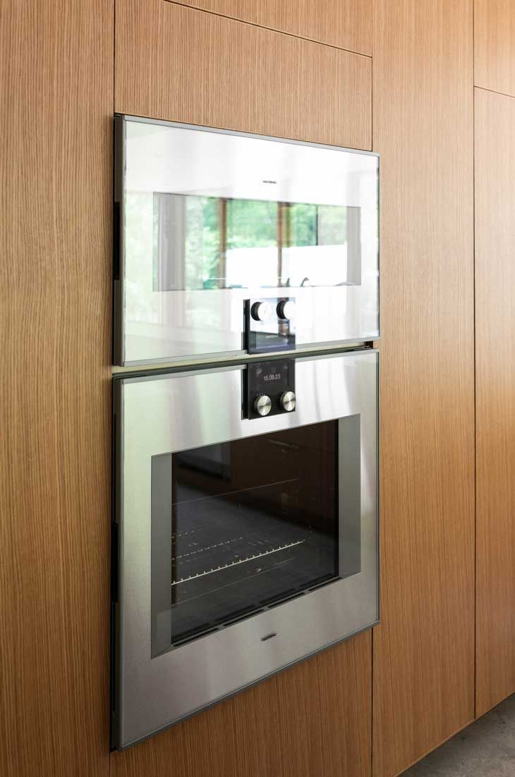 A stainless steel oven is mounted to a wooden wall in a kitchen.