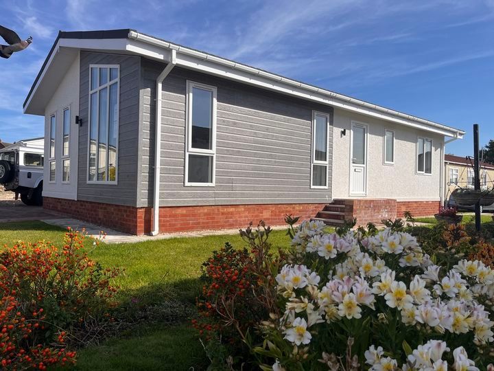 A mobile home is sitting in the middle of a lush green field with flowers in front of it.