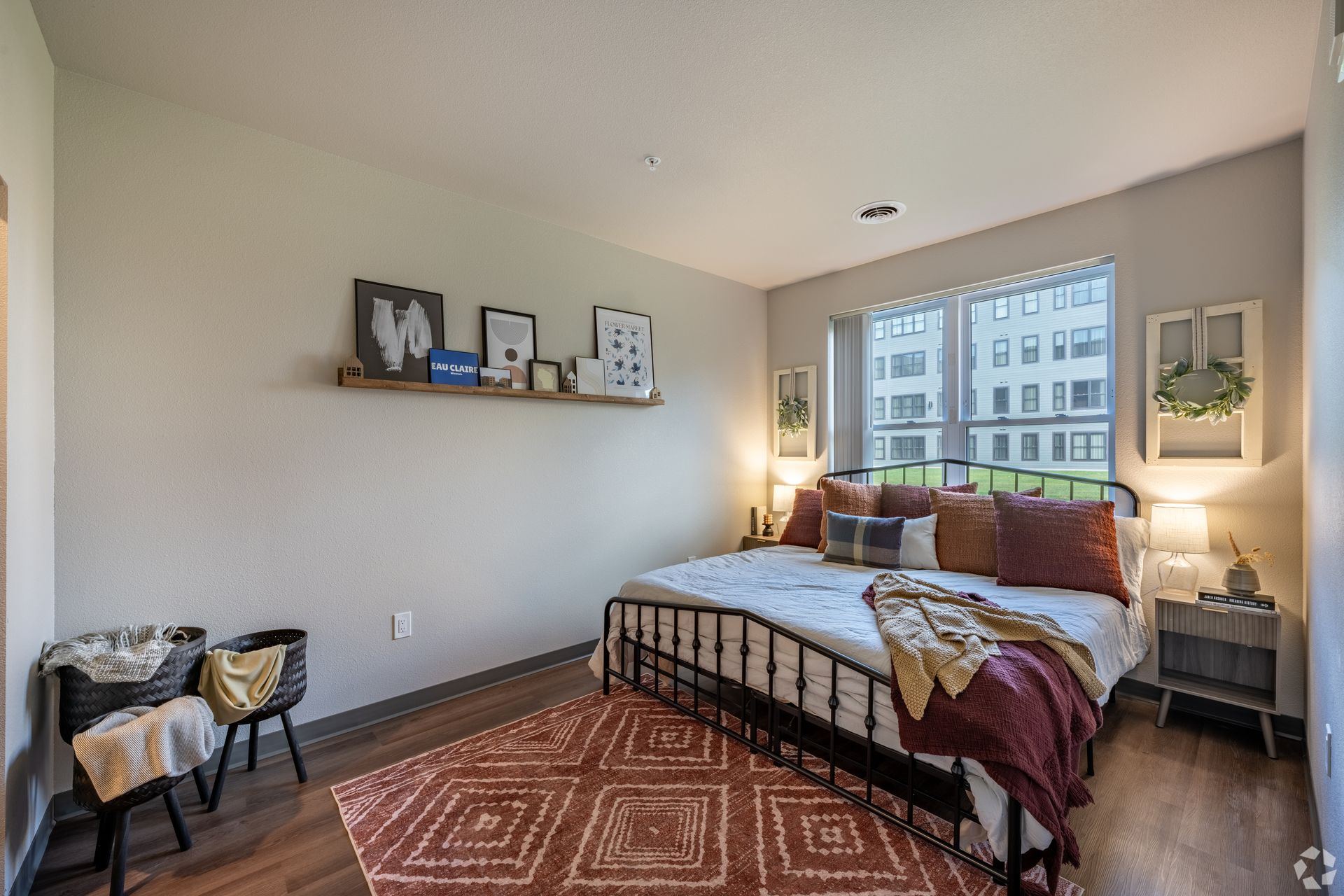 Bedroom with on large window, and orange area rug and art on the wall